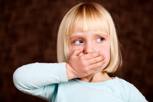 En blond flicka håller handen för munnen och tittar bort åt sidan